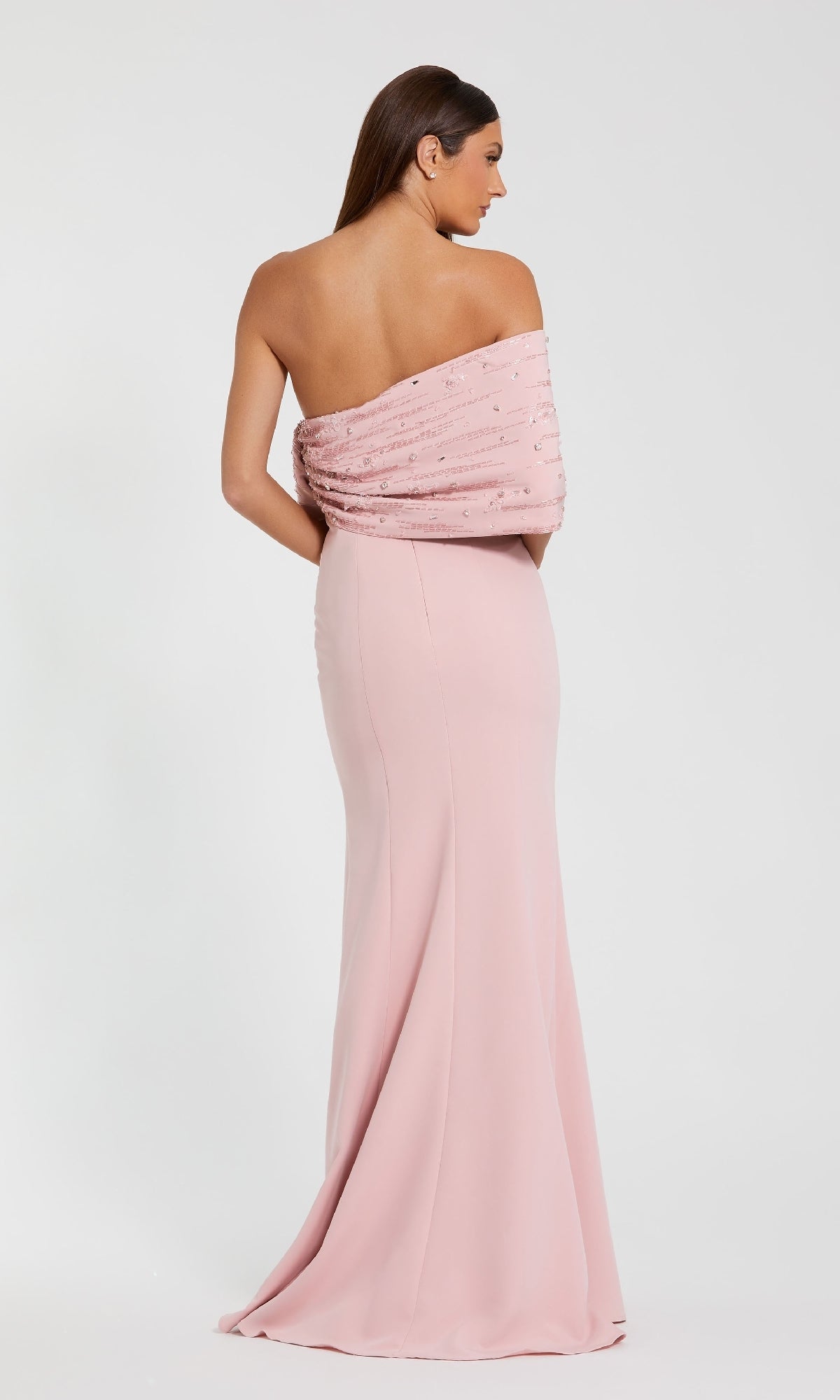 A woman in the Draped Long Pink Formal Dress: Mac Duggal 2305, a floor-length off-the-shoulder gown with beaded details, stands facing away against a plain white background.